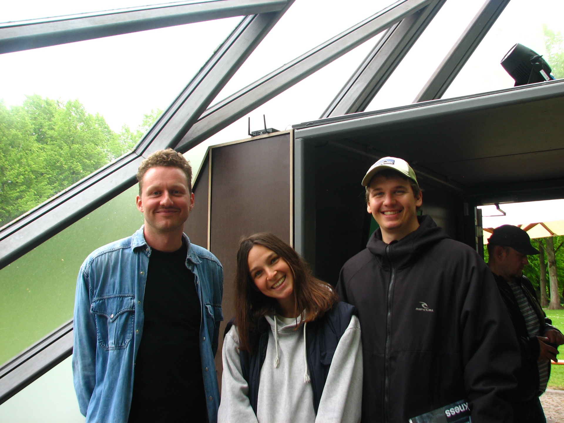 Three people smiling outside the triangular glass pavilion of Cisternerne.