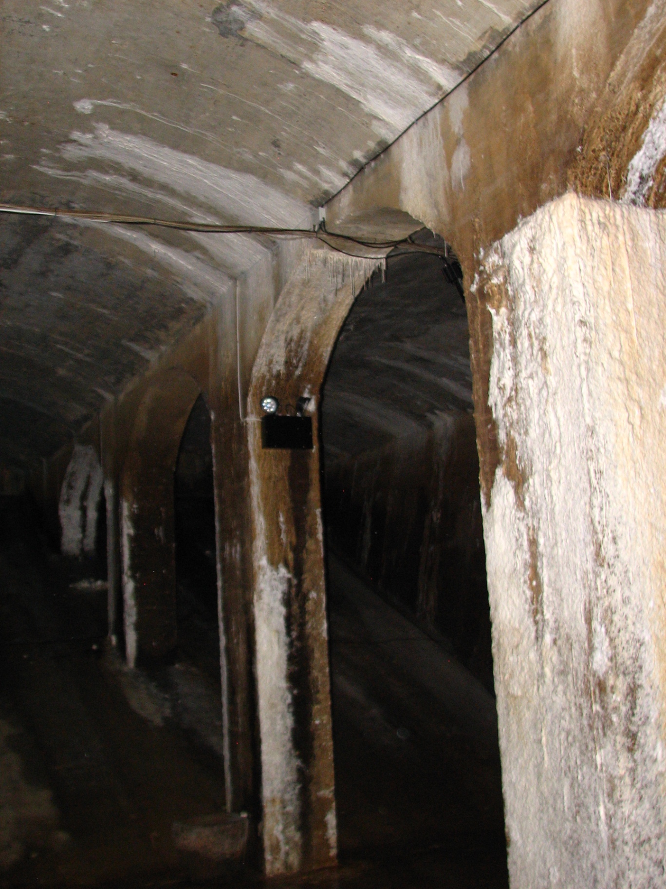 Dimly lit underground reservoir with vaulted concrete arches and mineral deposits streaking the columns.
