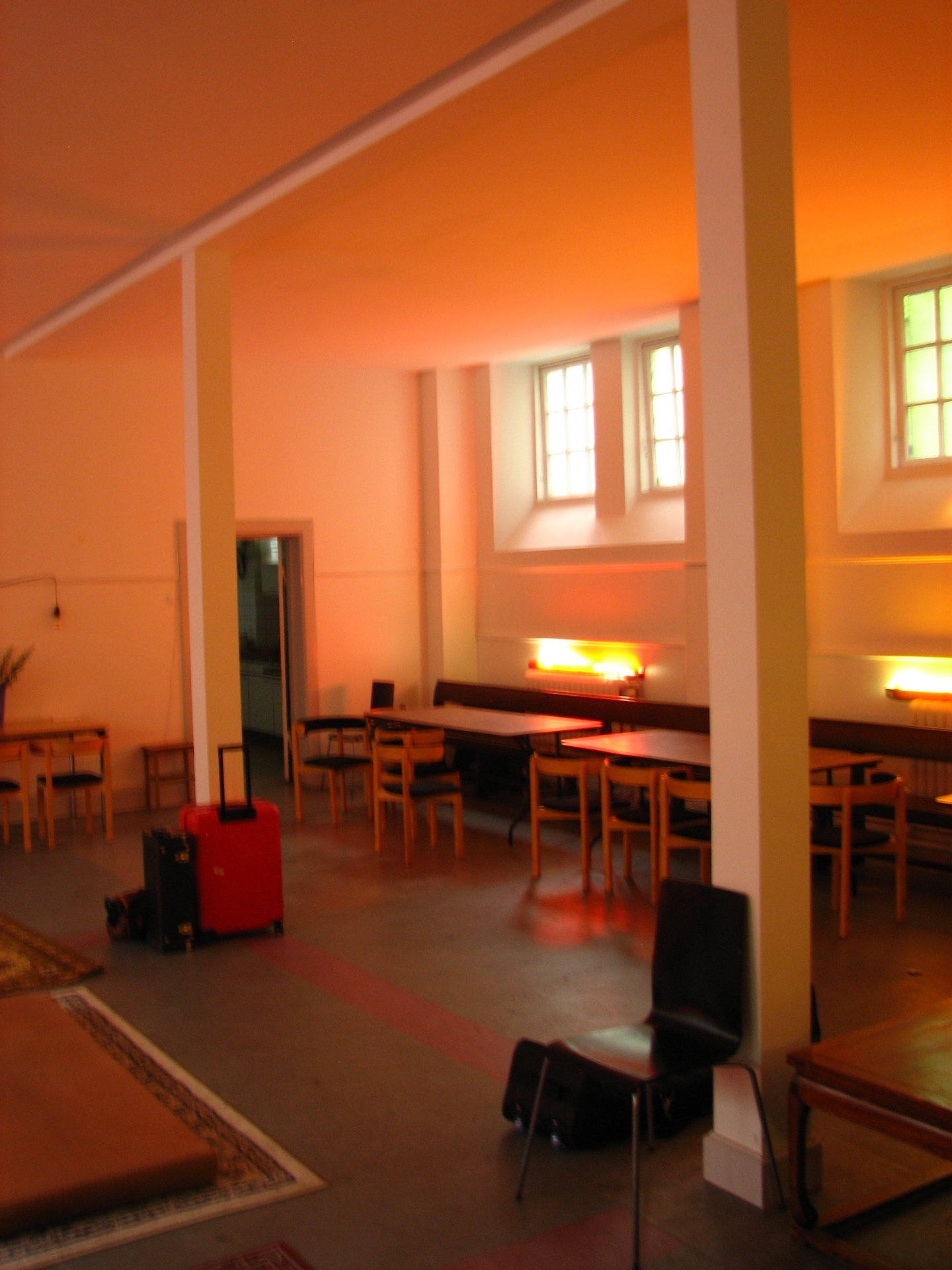 Side hall at KoncertKirken with wooden chairs and tables warmly lit by afternoon sun through grid windows.