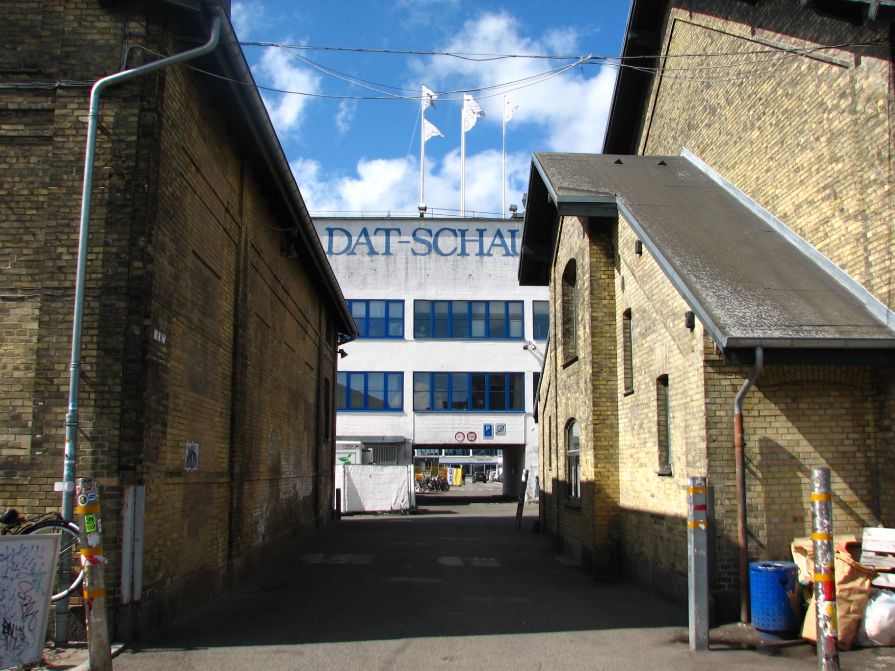 An alley between two yellow-brick warehouses in the Brune Kødby leading toward a white industrial building.
